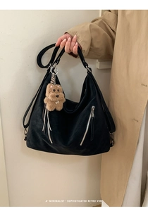 Detail of black large-capacity tote bag with silver zippers and a plush dog charm