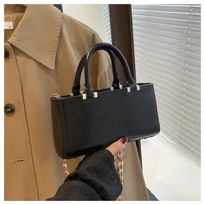 Close-up of black glossy leather handbag with gold metal accents and chain strap