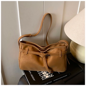Detail of caramel brown leather shoulder bag featuring a decorative buckle strap on a book