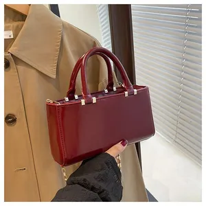 Close-up of glossy burgundy patent leather bag with gold metal studs and chain strap