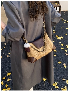 Detail of plaid crossbody bag with chain strap and heart charm on ginkgo leaves background