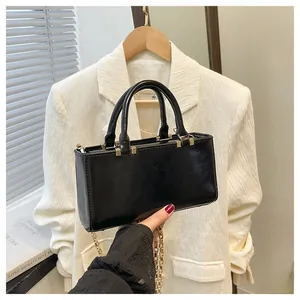 Detail of black faux leather tote with gold chain strap and polished metal accents