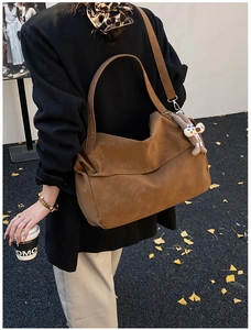 Detailed view of a brown suede tote bag with a cute charm accessory on a street setting