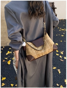 Macro view of plaid textured crossbody bag with golden chain and plush charm detail