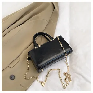 Detailed close-up of a black minimalist tote bag with a chunky gold chain strap