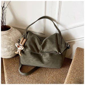 Detail of olive green tote bag with plush animal charm on a woven texture background