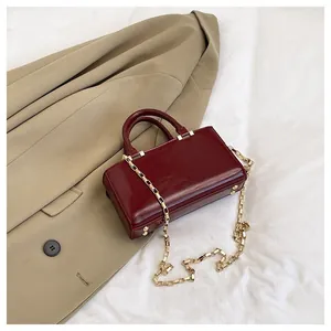 Detail view of wine red crossbody bag with gold chain and polished metallic feet