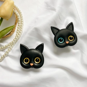 Detail of matte black cat phone grips with unique colored eyes on white silk fabric