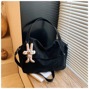 Close-up of black textured leather hobo bag with cute plush rabbit charm in natural sunlight