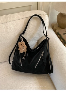 Detail of black suede hobo bag with silver zippers and a cute brown plush pendant