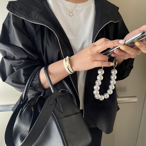 Detail showing large pearl phone strap with luxury clover necklace and black handbag