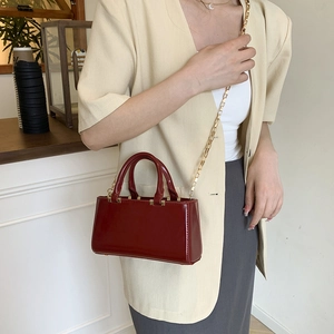 Minimalist deep red patent leather crossbody bag with elegant gold chain and top handle