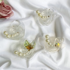 Detail of four heart-shaped resin hair clips with white pearls and green glitter on silk