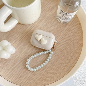 Detailed view of cream-colored AirPods case with heart charms and pearl wrist strap lanyard
