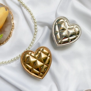 Macro shot of heart-shaped metal phone grips with quilted patterns in gold and silver