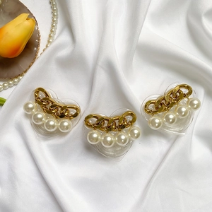 Close-up of heart-shaped phone stands with gold chains and pearls on white satin fabric