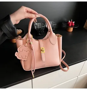 Detail showing pink pebble leather handbag with gold twist lock and dog-shaped charm