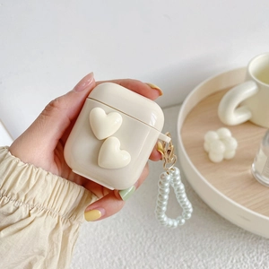Close-up of cream white AirPods case with 3D hearts and a pearl wrist strap accessory