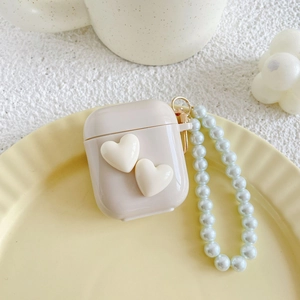 Detail of cream AirPods case with 3D hearts and white pearl wrist strap on tray