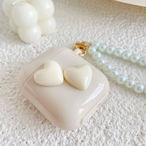 Detail view of cream-colored AirPods case with 3D hearts and white pearl lanyard strap