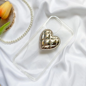 Detail of a transparent phone case with a gold heart grip on white silk background