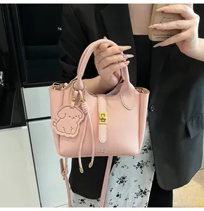 Close-up of pink litchi grain leather bucket bag with gold lock and dog charm pendant