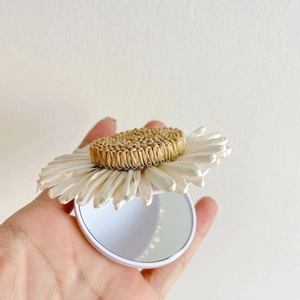 Detailed close-up of a daisy-shaped portable makeup mirror with woven center and white petals