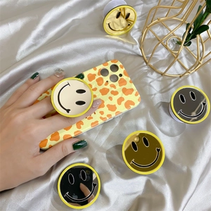 Close-up of yellow mirror smiley phone grip on an orange spotted phone case texture