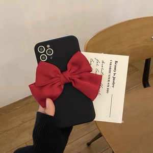 Matte schwarze iPhone-Hülle mit großer roter Satinschleife in gemütlicher Wohnumgebung
