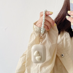 Creamy white AirPods case with 3D hearts and a pearl wrist strap on a trench coat background