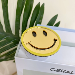 Detail showing a yellow smile face phone grip with mirror finish on a natural green background