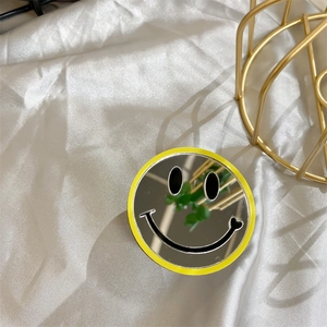 Detail view of yellow round smiley face mirror phone grip on white silk background