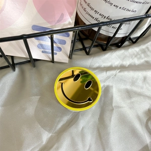 Detail of round yellow smiley face phone grip with reflective makeup mirror surface