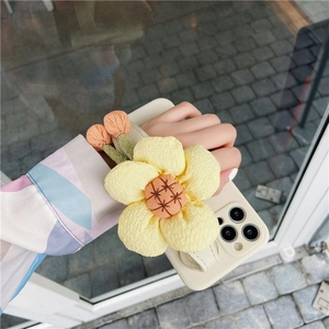 Detail of cream iPhone case featuring a large 3D yellow fabric flower and wrist strap