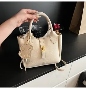 Detail view of cream lychee texture leather bucket bag with dog pendant and gold lock
