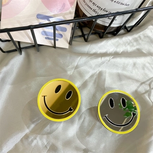 Close-up of a round yellow smiley face mirror phone grip on white silk fabric background