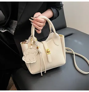 Close-up of cream lychee texture leather bucket bag with gold lock and puppy charm
