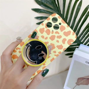 Close-up of a yellow giraffe-pattern phone case with a silver smiley face mirror stand