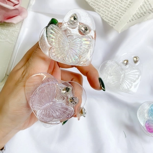 Transparent heart-shaped phone grip with butterfly relief and rhinestones on a white fabric