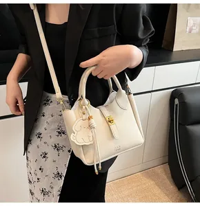 Close-up of white lychee leather bucket bag with gold lock and dog charm detail