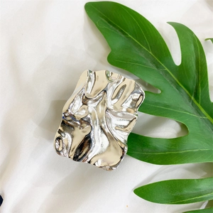 Detail shot of a liquid metal texture silver ring on white silk with a green leaf background