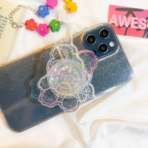 Detail of transparent glitter phone case with rainbow bear expanding grip on white fabric