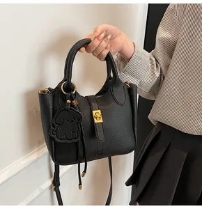 Detail of black lychee grain leather bucket bag with gold clasp and dog charm accessory