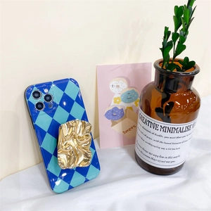 Detail of blue and green checkerboard phone case with a fold-out wrinkled gold metal stand