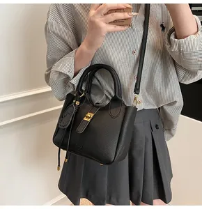 Detail of black lychee grain leather bucket bag with gold lock and key pendant worn by model
