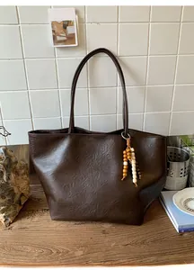 Detail of dark brown tote bag with pebble leather texture and colorful wooden bead tassel