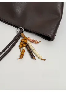 Detail of dark brown leather tote bag featuring a decorative wooden bead charm