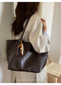 Detail of dark brown leather tote bag with wooden bead charm on a person's shoulder
