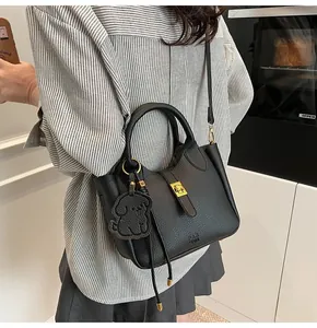 Detail of black lychee grain leather bucket bag with gold lock and dog charm on shoulder