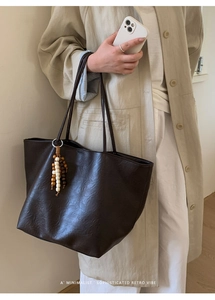 Detail of a large brown faux leather tote bag with vintage texture and beaded tassel charm